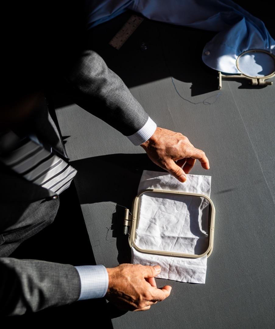 Welvin's hands and suit sleeves at work over linen in the atelier light